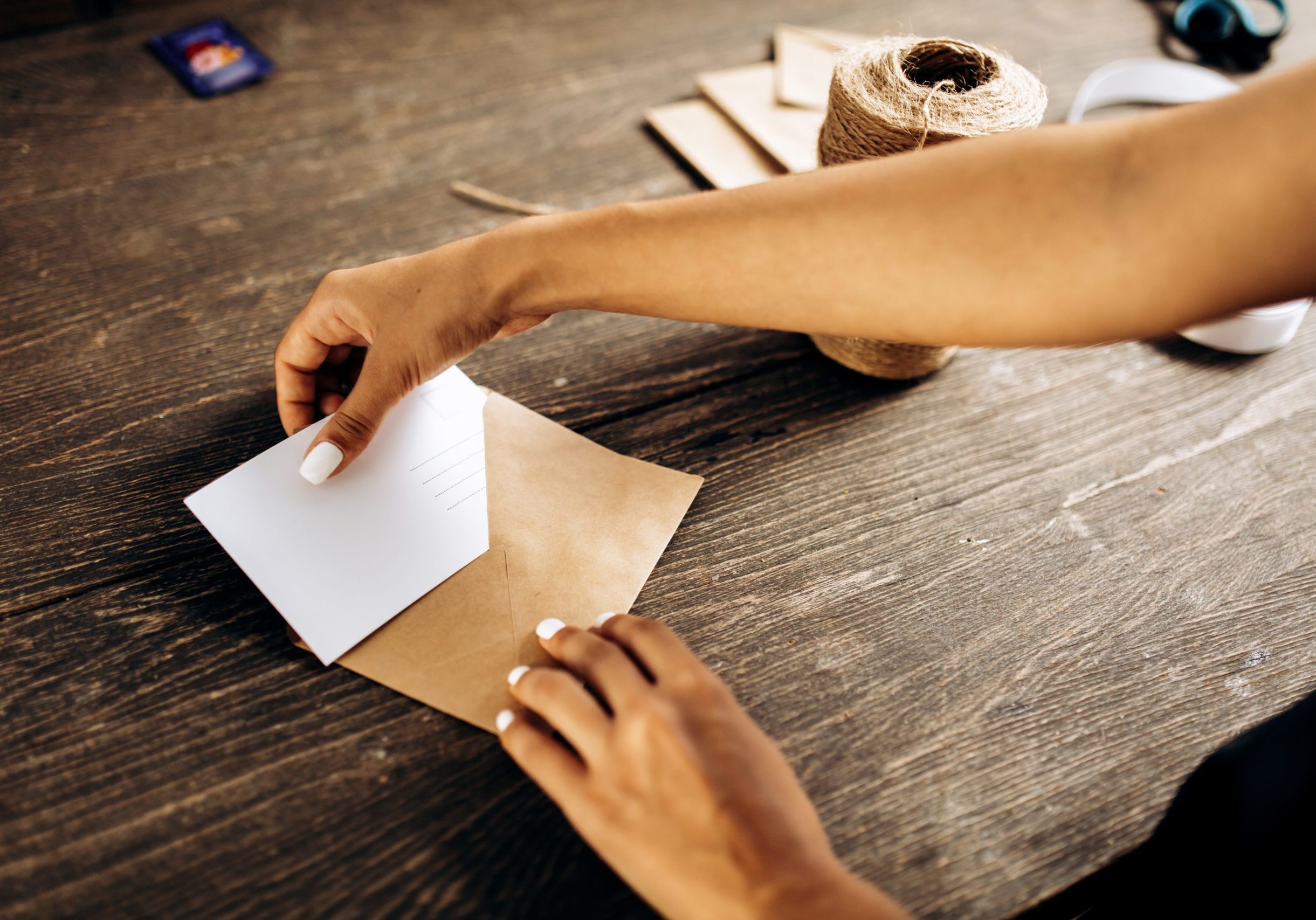 Florist is packing a postcard in an envelope with white ribbon on the wooden table .
